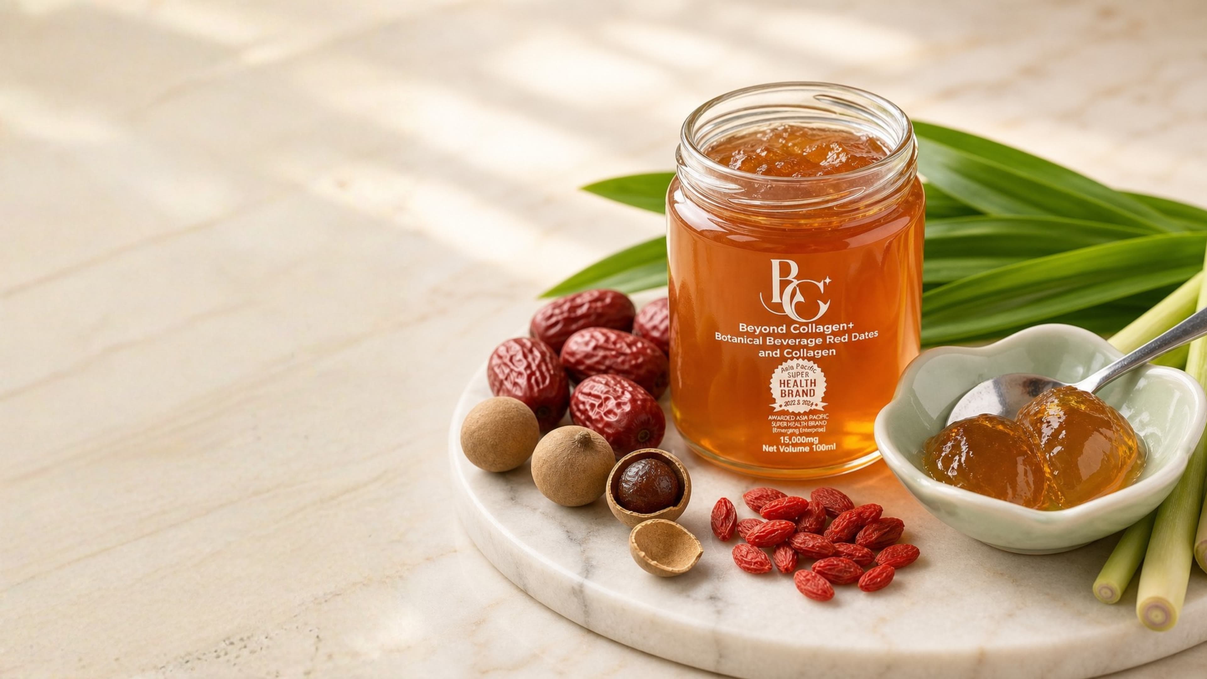 A jar of Beyond Collagen+ fish-scale collagen jelly on a marble board, with red dates, longan, goji, pandan and lemongrass, beside a dish of the set jelly
